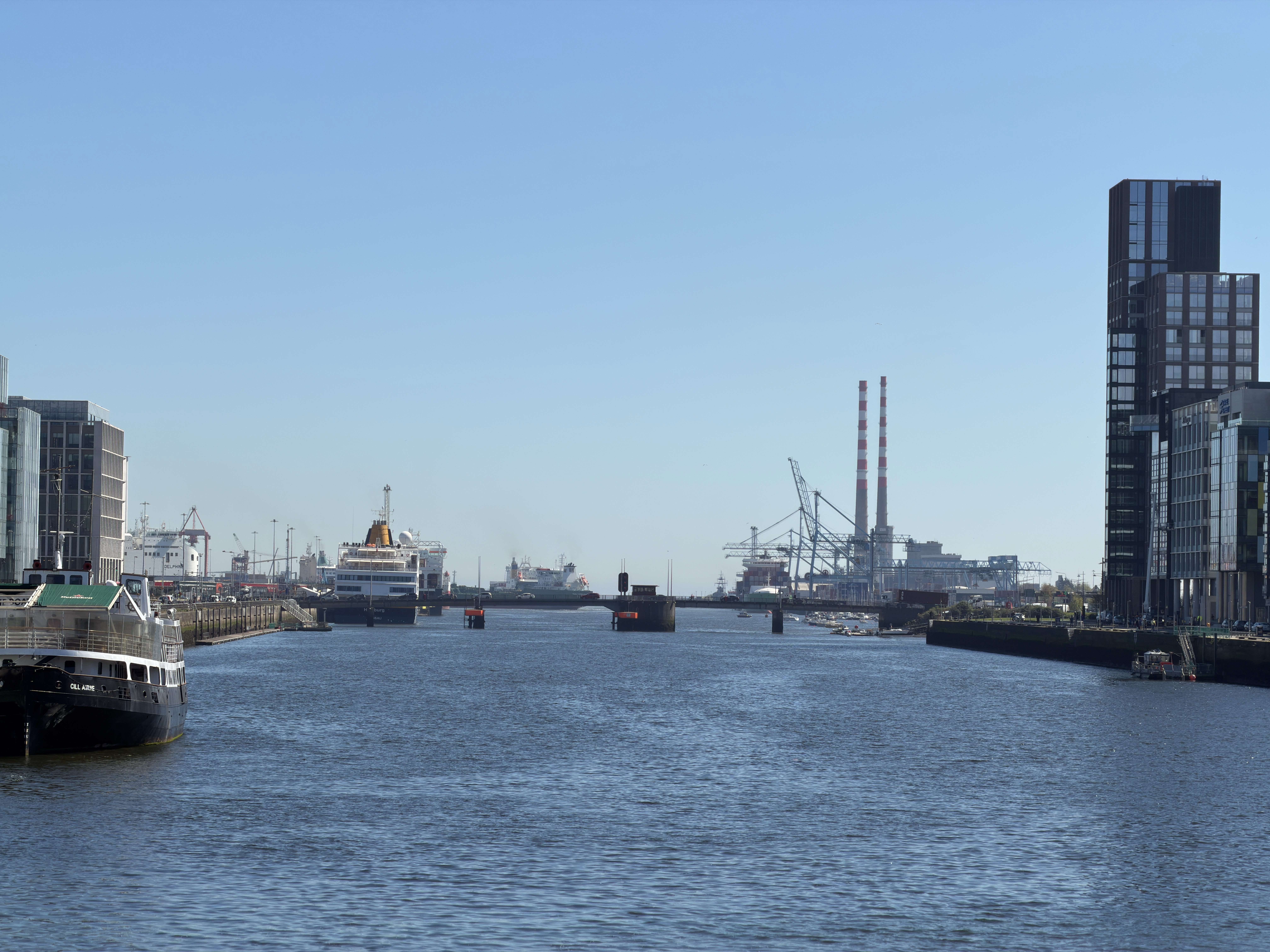 Ships, dockside buildings and cranes along Dublin waterfront under a blue sky.